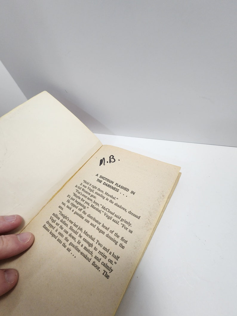 May include: A close-up of a book page with the text "A SHOTGUN FLASHED IN THE DARKNESS..."  The text continues with a story about a group of men in a Western setting.  The text reads "Hold it right there, Marshal."  "It was Virgil, standing in the shadows, dressed in full Western gear."  "Fun's over now, boys," McCloud said grimly.  "Maybe for you, Marshal," Virgil said.  "For us it's just beginning."