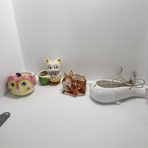 Puede incluir: Conjunto de cuatro macetas de cerámica vintage con un gato blanco, un ciervo marrón, una manzana blanca y una ballena blanca. Las macetas están en buen estado y tienen un estilo retro encantador.