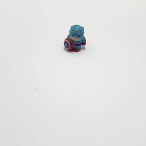 May include: A small blue and red plastic figurine of Captain America holding his shield. The figurine is about 2 inches tall.