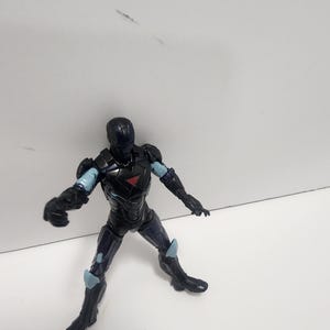 May include: Black and blue action figure of a superhero wearing a helmet and armor. The figure is posed in a dynamic stance with one arm raised and the other extended.