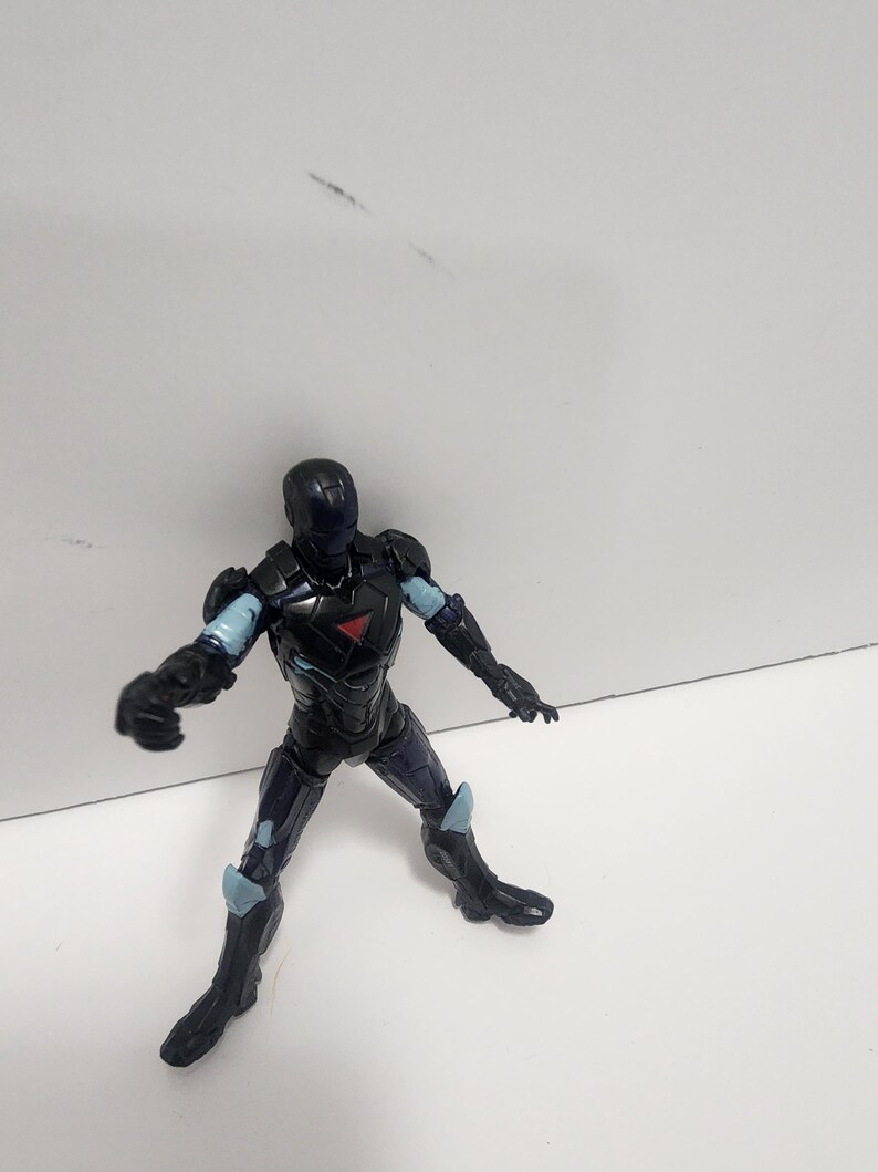 May include: Black and blue action figure of a superhero wearing a helmet and armor. The figure is posed in a dynamic stance with one arm raised and the other extended.