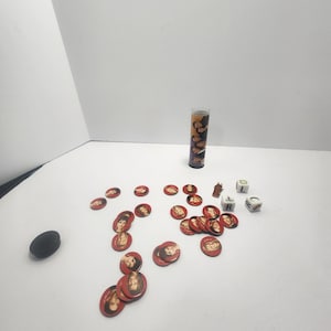 May include: A collection of game pieces, including red circular tokens with a woman's face, dice, a small wooden figure, and a tall glass tube with images. A black oval object is also present.