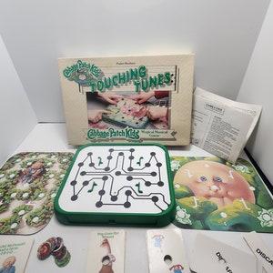 May include: Cabbage Patch Kids Touching Tunes Magical Musical Game board game with a green game board, colorful game cards, and a box with a Cabbage Patch Kid on the cover. The game is designed for ages 4 and up.