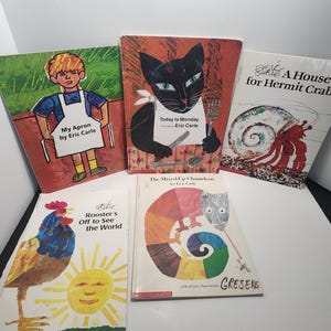 Puede incluir: Una colección de cinco libros infantiles de Eric Carle. Los libros presentan ilustraciones coloridas de un niño con un delantal, un gato negro, un camaleón, un gallo y un cangrejo ermitaño. Los títulos de los libros son "Mi delantal", "Hoy es lunes", "El camaleón mezclado", "El gallo sale a ver el mundo" y "Una casa para el cangrejo ermitaño".