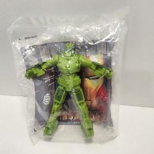 May include: Green plastic Iron Man action figure in a clear plastic bag with a cardboard backing. The backing has a picture of Iron Man and the words "Iron Man 2".