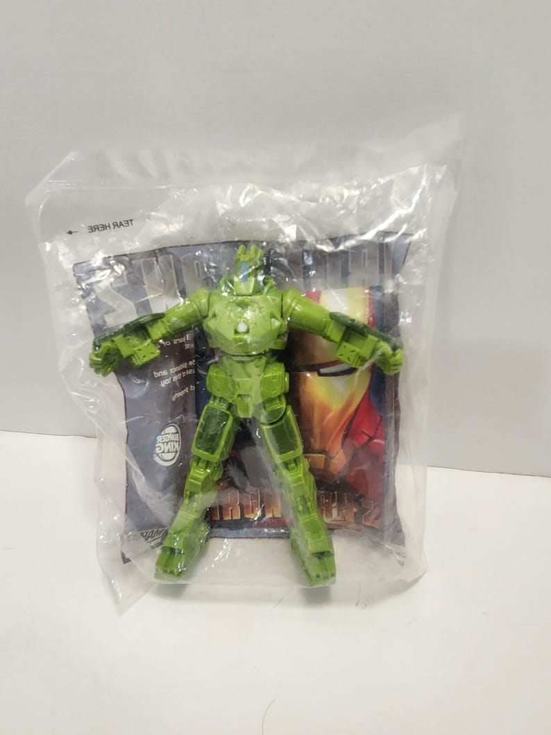 May include: Green plastic Iron Man action figure in a clear plastic bag with a cardboard backing. The backing has a picture of Iron Man and the words "Iron Man 2".