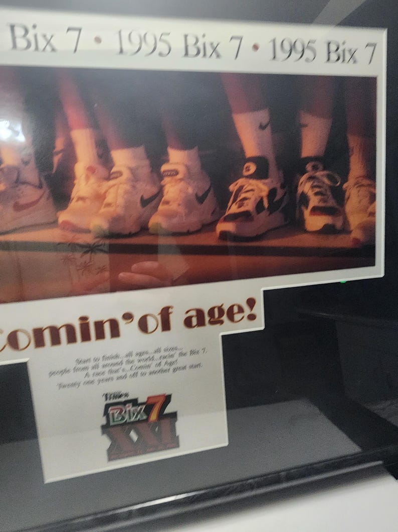 Peut inclure: Publicit&eacute; encadr&eacute;e pr&eacute;sentant plusieurs paires de baskets Nike blanches et noires. Le texte "Bix 7 - 1995 Bix 7" est affich&eacute; en haut. La phrase "Comin' of age!" est &eacute;galement visible, ainsi que du texte suppl&eacute;mentaire et le logo Bix 7.