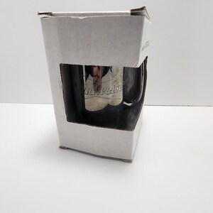 Puede incluir: Una caja de cart&oacute;n blanca con una taza de acero inoxidable plateada en su interior. La taza tiene el logotipo de Budweiser grabado en el lateral.