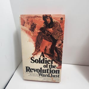 Pode incluir: Um livro de bolso intitulado A Soldier of the Revolution de Ward Just. A capa apresenta uma ilustração de uma pessoa sentada numa rocha numa paisagem desértica com um cavalo e um cavaleiro ao fundo. O texto inclui o título e o autor.