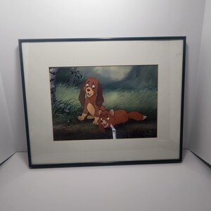 May include: Framed artwork featuring a cartoon illustration of a dog and a fox in a grassy field. The dog is brown and tan, and the fox is reddish-brown. The artwork is set against a backdrop of green foliage and a blue sky.
