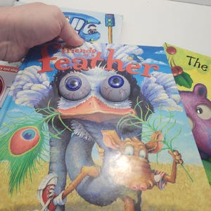 Puede incluir: Una pila de libros infantiles. El libro superior, titulado "Friends of a Feather", presenta una ilustraci&oacute;n de dibujos animados de una criatura con ojos grandes y saltones y un personaje parecido a un burro con zapatillas rojas.