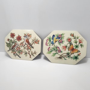 Puede incluir: Dos placas de pared octogonales de cerámica con diseños florales y de pájaros. La primera placa presenta un pájaro marrón con cabeza azul y un pequeño pájaro marrón en una rama con flores rosas y hojas verdes. La segunda placa presenta una mariposa azul y amarilla y una mariposa marrón con alas naranjas en una rama con flores rosas y moradas y hojas verdes.
