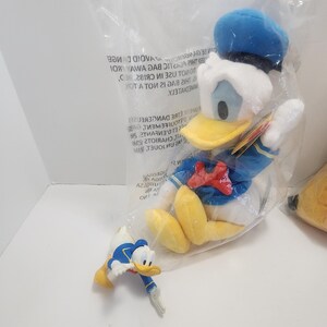 Pu&ograve; includere: Un peluche di Paperino in un sacchetto di plastica trasparente, con cappello da marinaio blu, giacca e papillon rosso. &Egrave; presente anche una piccola statuina di Paperino.