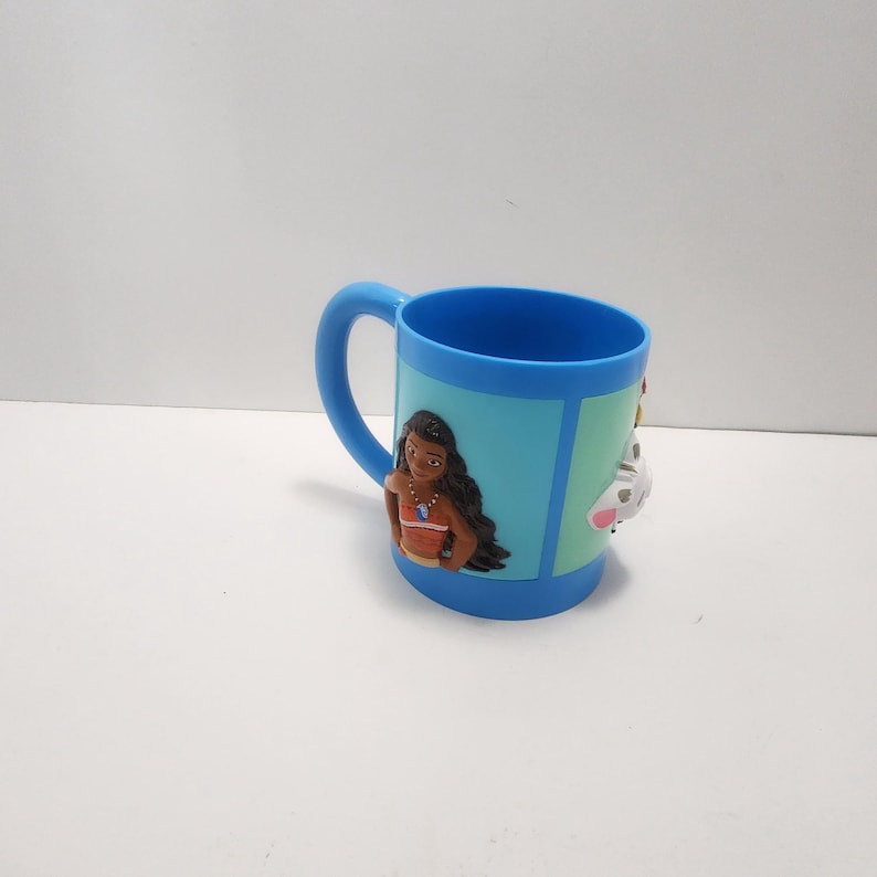 May include: A blue plastic mug featuring a cartoon character design. The mug has a blue handle and a light blue background with a cartoon character on the front. The mug is designed for children.