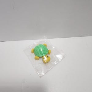 May include: A small green and yellow plastic turtle eraser in a clear plastic bag.