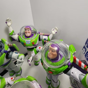 May include: Four Buzz Lightyear action figures from the Toy Story franchise. The figures are green, white, and purple with a clear plastic dome over the head. The figures have articulated arms and legs.