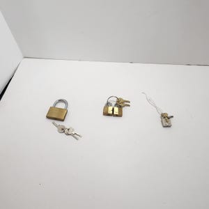 May include: A collection of padlocks and keys including one large brass padlock with a silver shackle and two keys, two smaller brass padlocks joined together with keys, and one small silver-toned padlock with a single key attached by a string.