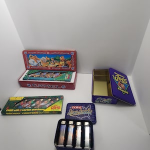Może przedstawiać: Zestaw vintage puszek na zapalniczki do papierosów z różnymi markami, w tym Camel, Doral i Smokin' Joe's Racing. Puszki są puste i mają kolorowe grafiki.