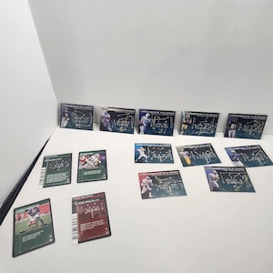 Puede incluir: Un conjunto de cromos de fútbol con imágenes de jugadores y diagramas de juego. Las tarjetas tienen un fondo oscuro con texto blanco y amarillo. Algunas tarjetas son verdes, otras granates.