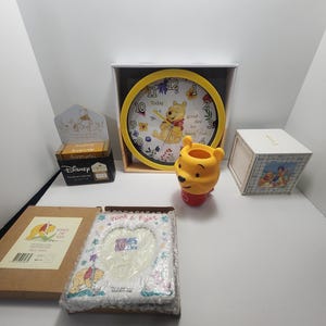 May include: A Winnie the Pooh themed set of home decor items including a clock, a picture frame, a small box, and a figurine. The clock features Winnie the Pooh playing a musical instrument with the text "Today is a good day for being Pooh". The picture frame is decorated with Winnie the Pooh and Piglet. The small box is decorated with Winnie the Pooh and Tigger. The figurine is a yellow Winnie the Pooh.