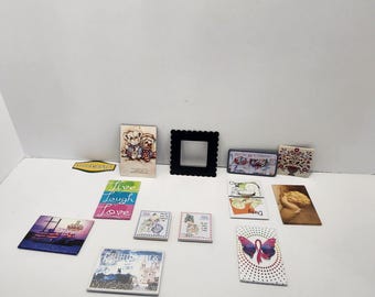 Könnte beinhalten: Eine Sammlung dekorativer Artikel, darunter kleine quadratische Fliesen mit verschiedenen Designs, ein schwarzer quadratischer Rahmen und ein Schild mit der Aufschrift "Live Laugh Love". Die Fliesen zeigen Bilder von Schmetterlingen, Gebäuden und anderen Grafiken.