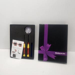 May include: A black gift box with a purple ribbon and the text "Refreshing your phone." Inside, a set of repair tools, including screwdrivers with red, yellow, and blue handles, and a small clear suction cup.