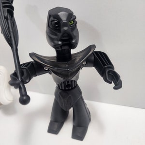 May include: Black robot toy with a green eye and a black staff. The robot has a detailed design and is posed standing with its arms outstretched.