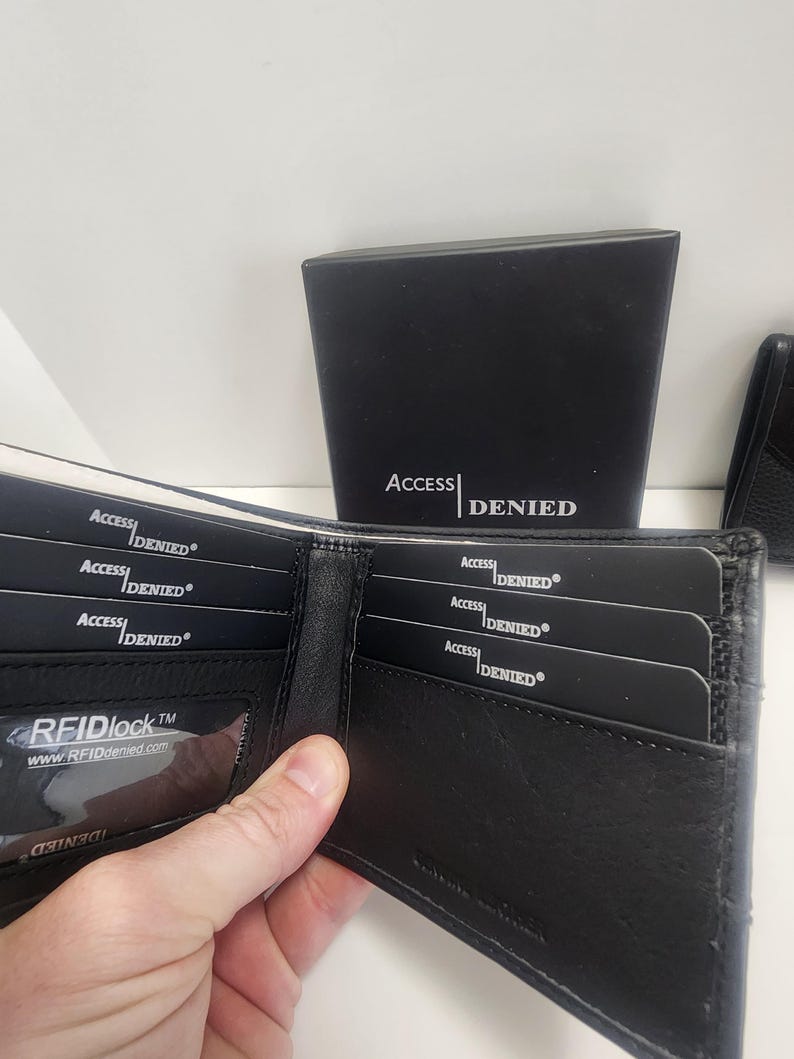May include: Black leather wallet with multiple card slots, some containing cards with "ACCESS DENIED" printed on them. The wallet is open, revealing the interior. A black box with "ACCESS DENIED" is in the background.