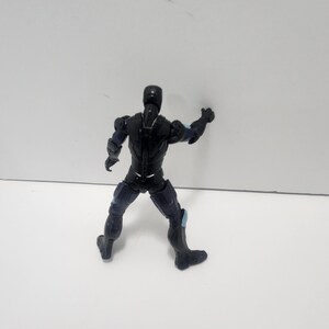 May include: Black action figure with blue accents, standing on a white surface. The figure is posed with one arm raised and the other arm at its side.
