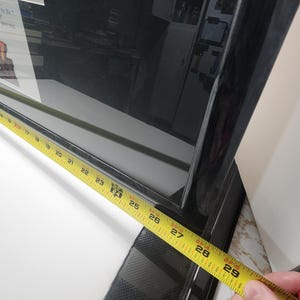 Peut inclure: Un cadre noir avec un ruban &agrave; mesurer jaune indiquant une longueur de 71 cm. Le cadre a une finition brillante et un motif textur&eacute; sur le bord inf&eacute;rieur. Le mot "age!" est visible dans le coin sup&eacute;rieur gauche.