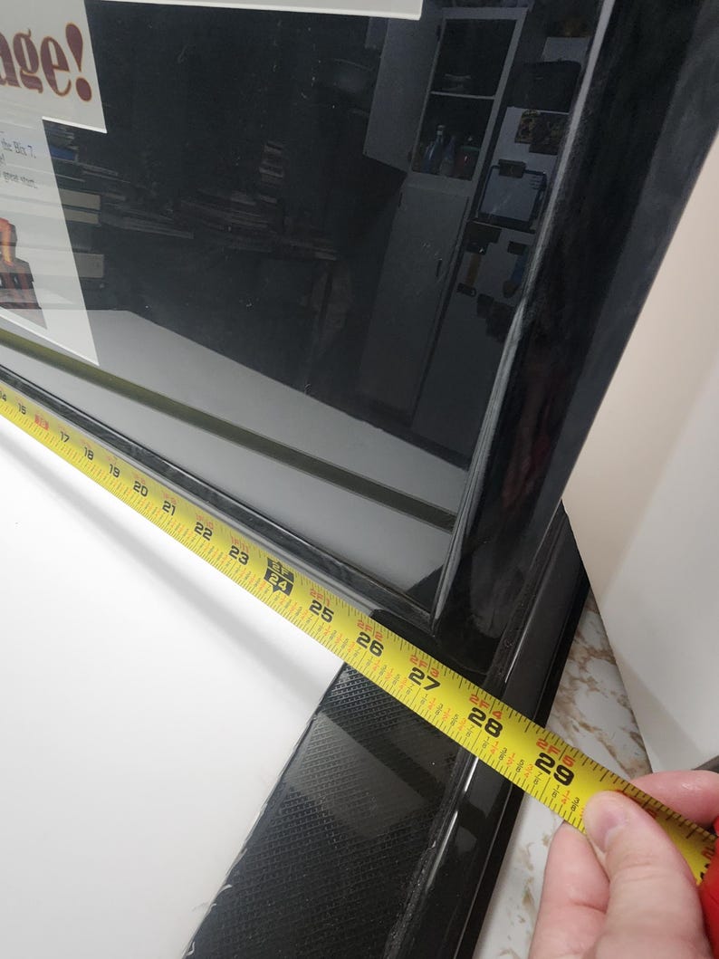 Peut inclure: Un cadre noir avec un ruban &agrave; mesurer jaune indiquant une longueur de 71 cm. Le cadre a une finition brillante et un motif textur&eacute; sur le bord inf&eacute;rieur. Le mot "age!" est visible dans le coin sup&eacute;rieur gauche.