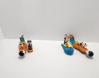 Puede incluir: Cuatro figuras de plástico de Goofy en diferentes poses. Un Goofy está en una patineta, otro en una tabla de surf y dos sostienen bolas de bolos.