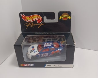Op de afbeelding: Een blauwe en witte speelgoedauto van metaal met nummer 12 en het Mobil 1 logo. De auto is een Ford Taurus en maakt deel uit van de Hot Wheels Racing Track Edition-serie.
