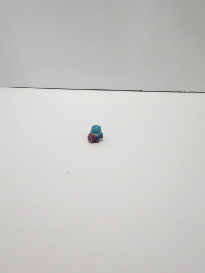 May include: A small blue and red plastic figurine of Captain America, holding his shield.