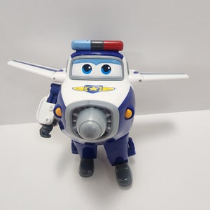 May include: A blue and white toy airplane with a red and blue light on top. The airplane has a yellow star on its chest and a gray propeller. The toy is in a robot-like pose with its legs and arms extended.