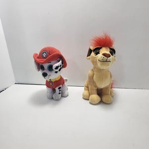 May include: Two plush toys, a white and black dalmatian wearing a red fire hat and a tan lion with a red mane.