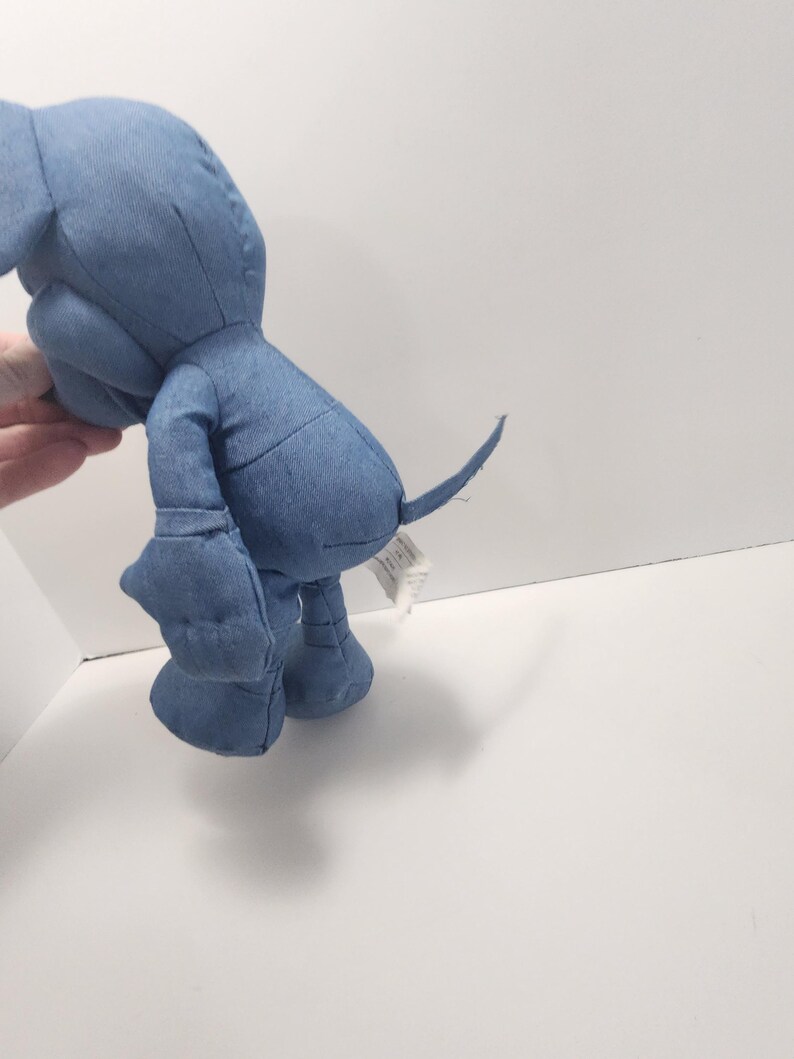 Puede incluir: Un peluche de elefante de mezclilla azul. El animal de peluche tiene patas grandes y redondeadas, una larga trompa y una peque&ntilde;a cola. El elefante est&aacute; hecho de tela de mezclilla azul claro y tiene costuras cosidas.