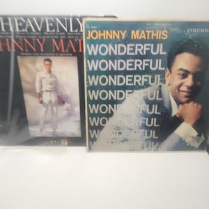 May include: Two vintage vinyl record albums. One album cover features the text "Heavenly" and "Johnny Mathis". The other album cover features a portrait of Johnny Mathis and the word "Wonderful" repeated multiple times.