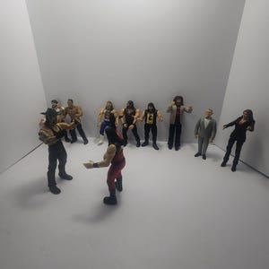 May include: A collection of professional wrestling action figures, posed in a white studio. The figures are dressed in wrestling attire, including hats and jackets. The figures are in various poses, as if they are in a wrestling match.