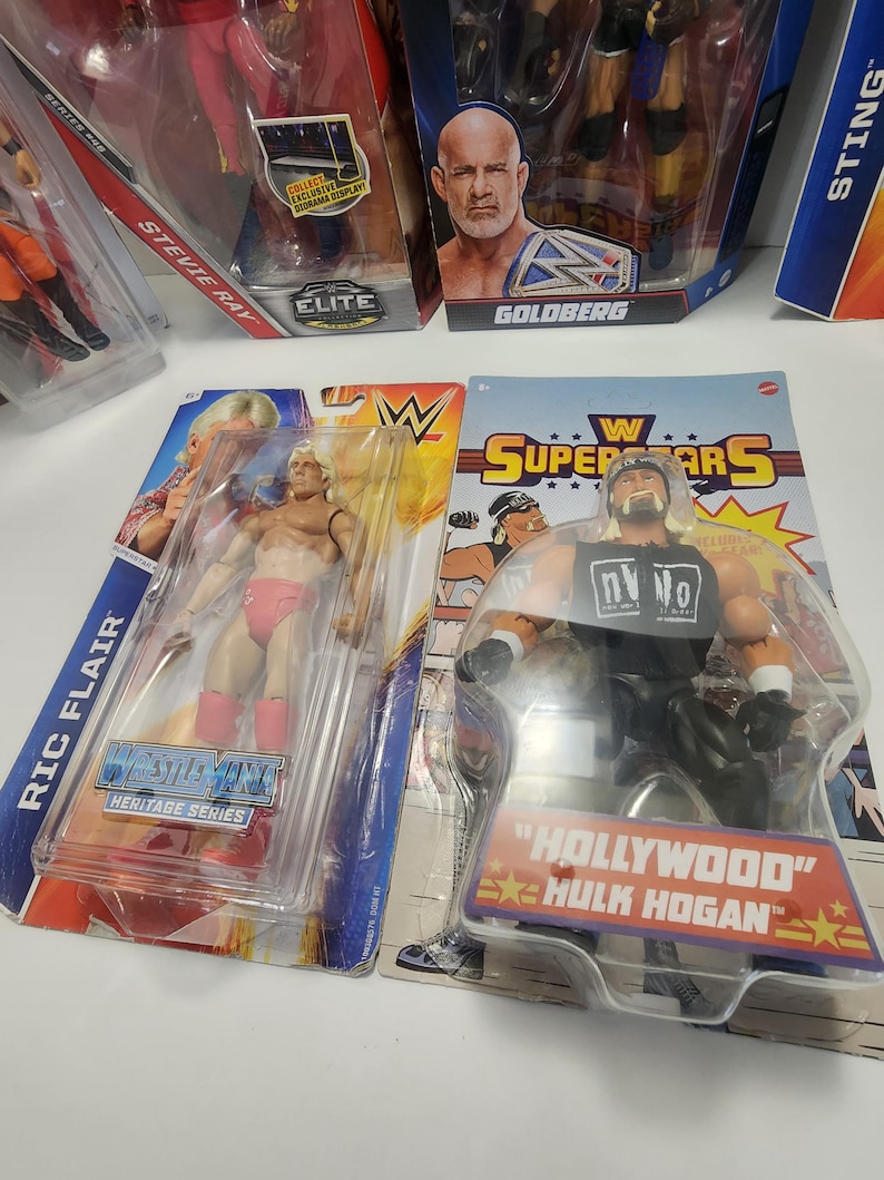 Op de afbeelding: Een verzameling WWE worstel action figures, waaronder Ric Flair, Hulk Hogan, Goldberg en Sting. De figuren zijn verpakt in hun originele dozen, die kleurrijke afbeeldingen en logo's bevatten.