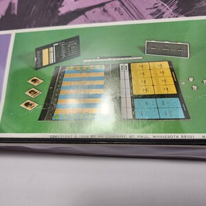 Peut inclure: Un plateau de jeu avec une grille de cases, une feuille de score et des d&eacute;s. Le plateau de jeu est vert et bleu, et la feuille de score est jaune. Les d&eacute;s sont blancs. Le jeu s'appelle "Le Jeu de la Vie".