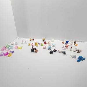 May include: A collection of small, colorful animal figurines. The figurines are made of plastic and are about 1 inch tall. They include a variety of animals, such as a cat, a dog, a bird, a fish, a turtle, a rabbit, a unicorn, a dolphin, an owl, a pig, a cow, a horse, a sheep, a goat, a monkey, a bear, a lion, a tiger, a zebra, a giraffe, an elephant, a rhinoceros, a hippopotamus, a crocodile, a snake, a lizard, a frog, a butterfly, a ladybug, a bee, a spider, a worm, a snail, a mushroom, a flower, a tree, a rock, a cloud, a star, a moon, and a sun.