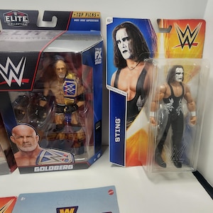 Op de afbeelding: Drie WWE-actionfiguren in hun verpakking. De figuren zijn Goldberg, Sting en een tweede Sting-figuur. De verpakking is rood, zwart en wit met het WWE-logo. De figuren dragen allemaal worstelkleding.