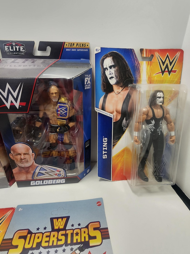Op de afbeelding: Drie WWE-actionfiguren in hun verpakking. De figuren zijn Goldberg, Sting en een tweede Sting-figuur. De verpakking is rood, zwart en wit met het WWE-logo. De figuren dragen allemaal worstelkleding.