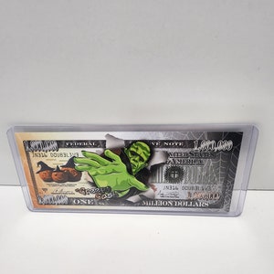 Może przedstawiać: Fantazyjny banknot o nominale 1 000 000 dolarów z wizerunkiem zielonego potwora i dyniami. Na banknocie widnieje napis "Creepy Cash" i "Jeden milion dolarów".