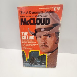 May include: A red and white paperback book cover with the title "The Killing" and the text "Marshal McCloud follows the tortuous trail of a ruthless gang on a million-dollar heist!"  The cover features a photo of a man wearing a brown cowboy hat and a brown jacket. The book is part of the "3 In A Dynamite Series" based on the NBC-TV show "McCloud".