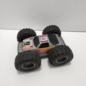 Puede incluir: Un camión monstruo de juguete plateado con neumáticos negros y el número "76" en el lateral. El camión tiene las palabras "ZOOM" y "4X4" impresas.
