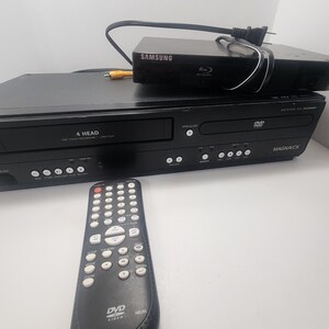 K&ouml;nnte beinhalten: Schwarzer DVD-Player mit Fernbedienung. Der DVD-Player verf&uuml;gt &uuml;ber eine 4-Kopf-One-Touch-Aufnahmefunktion mit langer Spielzeit. Der DVD-Player ist von Magnavox.
