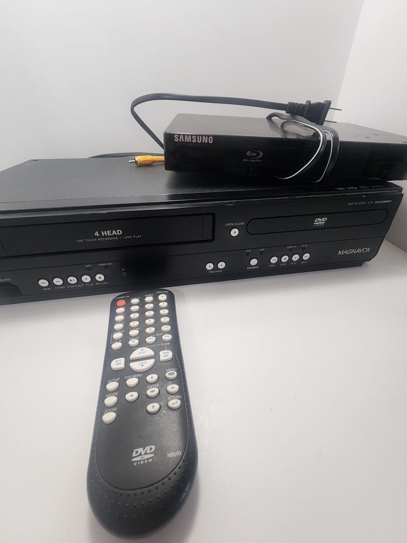 K&ouml;nnte beinhalten: Schwarzer DVD-Player mit Fernbedienung. Der DVD-Player verf&uuml;gt &uuml;ber eine 4-Kopf-One-Touch-Aufnahmefunktion mit langer Spielzeit. Der DVD-Player ist von Magnavox.
