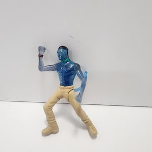 May include: A blue translucent action figure of a character from the movie Avatar. The figure is wearing tan pants and has a blue tail.